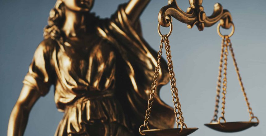 Figure of Justitia or Justice holding the scales of justice with close up focus to the scales symbolic of the law over grey